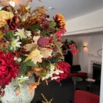 Decoratief bloemstuk in vaas in de kleuren rood, oranje en wit, tussen de groene bladeren