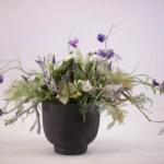 Decoratief bloemstuk in een antraciete vaas in de kleuren paars en wit met groene bladeren