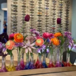 Gekleurde smalle vaasjes op een rij met elk een bundel van 2 of 3 kleurrijke bloemen