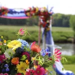 Boeket in close up van kleurrijke bloemen met in de verte een prieel van gekleurde bloemen en paarse doeken