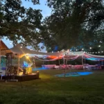 Grote tuin met een overkapping van wit doek in de schemering, aangevuld met feestelijke verlichting