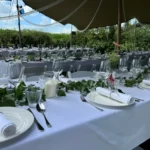 Lange rijen witte ingedekte tafels, met groene bladerstroken op elke rij tafels