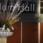 Kunstzinnig gedecoreerde witte vaas op een statief met witte takken en groene bladeren met witte bloemen