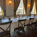 Feestelijke aankleding van een lange ingedekte tafel met wit tafelkleed, voorzien van diverse kleine bloemstukken