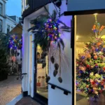 Gedecoreerde voorgevel van een winkel met hangende potten met hangende dennenappels met gouden linten in een kleurrijk, voornamelijk paars, geheel