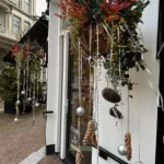 Gedecoreerde voorgevel van een winkel met hangende potten met hangende dennenappels en kerstballen met hierin hulst met rode besjes